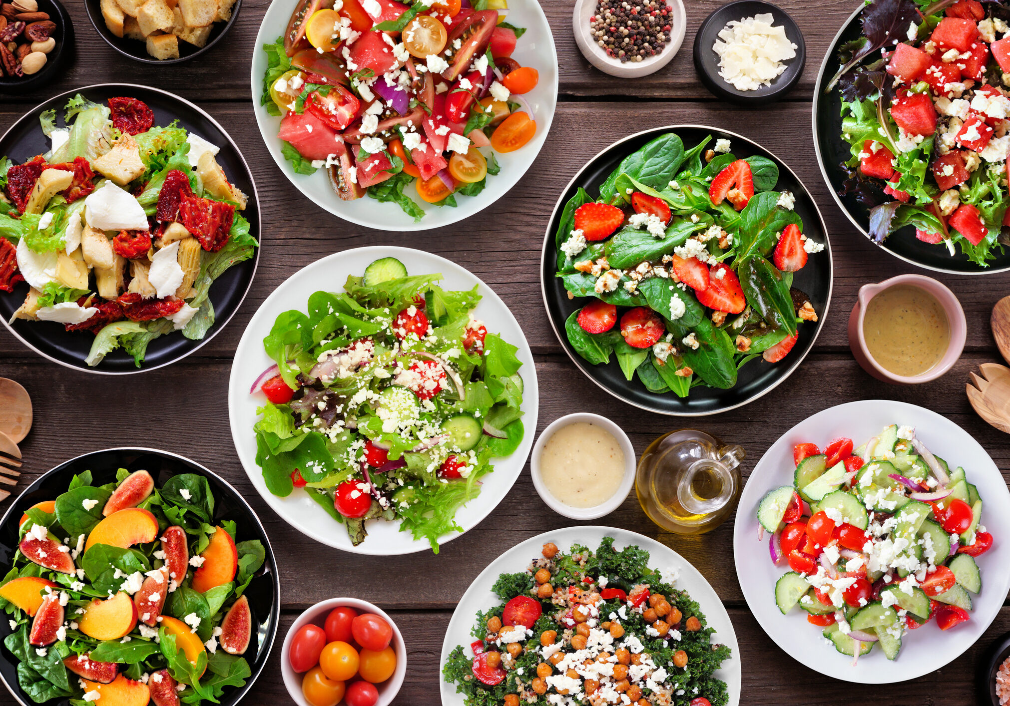 Variety of delicious fresh salads. Above view table scene on a dark wood background.