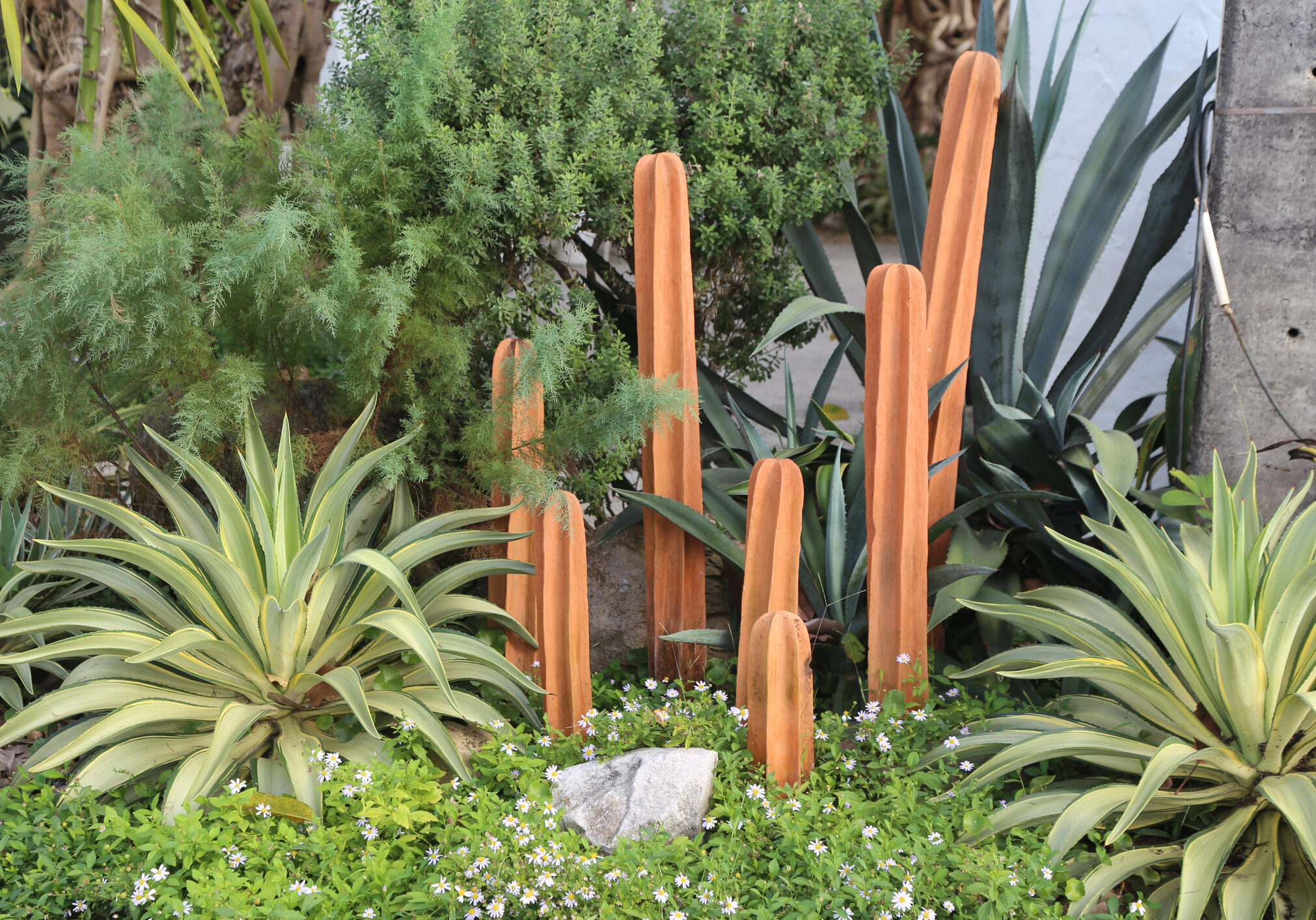 A garden with several wooden stakes shaped like cacti, placed in the center of green plants and flowers.
